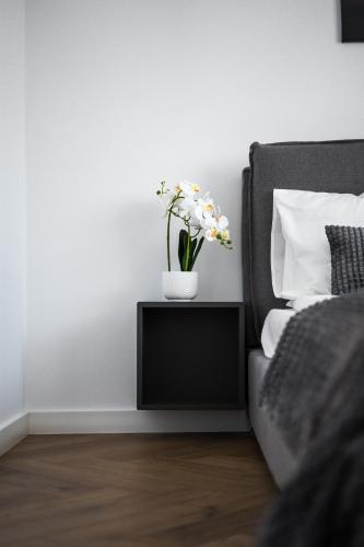 a bed with a vase of flowers on a side table at Sky9 Apartment in Odorheiu Secuiesc