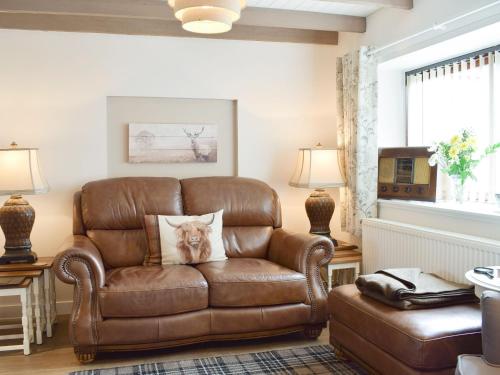 Una silla de cuero marrón en una sala de estar con un perro sobre una almohada. en Horseshoe Cottage, en Fife