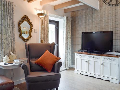 sala de estar con silla y TV de pantalla plana en Horseshoe Cottage, en Fife