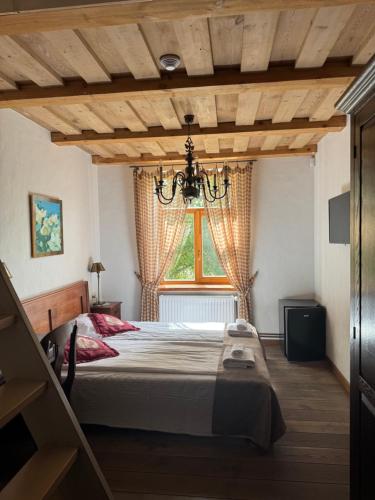 a bedroom with a bed with a chandelier and a window at Pilsberģu krogs in Jūrkalne