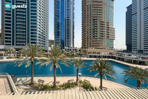 a pool with palm trees in a city with tall buildings at HiGuests - Fabulous Duplex With Breathtaking Lake Views in Dubai