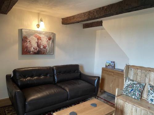 a living room with a leather couch and a painting at Penny Black Cottage in Ingleton