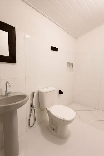 a white bathroom with a toilet and a sink at Pousada Vilarejo in Caraíva