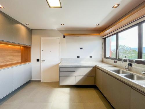a kitchen with white cabinets and a large window at Cobertura Pé na Areia - Enxoval Completo Riviera in Riviera de São Lourenço