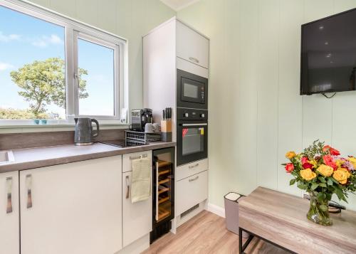 a kitchen with white cabinets and a table with a vase of flowers at Calvesland Hideaway in Manorbier