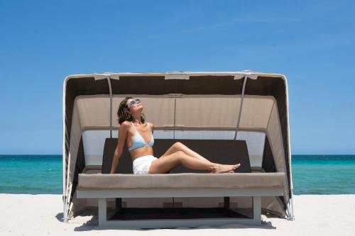 a woman sitting in a beach bed on the beach at Kimpton Surfcomber Hotel by IHG in Miami Beach