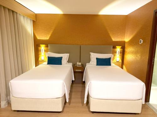 two beds in a hotel room with white sheets and blue pillows at Wyndham Sao Paulo Ibirapuera Convention Plaza in Sao Paulo