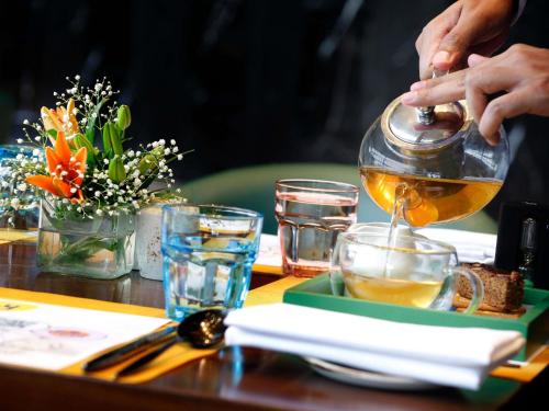 a person pouring a pot of tea on a table at Novotel Kolkata Hotel and Residences in Kolkata
