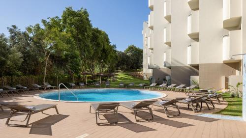 a swimming pool with lounge chairs and a building at Holiday Inn Algarve Albufeira by IHG in Albufeira