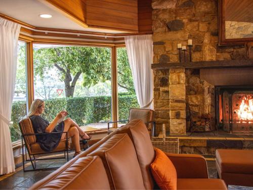 a woman sitting in a chair in a living room with a fireplace at Mercure Hunter Valley Gardens in Pokolbin