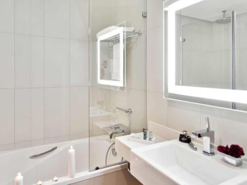 a white bathroom with a sink and a tub and a mirror at Novotel Abu Dhabi Gate in Abu Dhabi