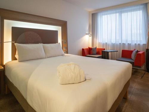 a hotel room with a large white bed with a white bag on it at Novotel London Brentford in Brentford