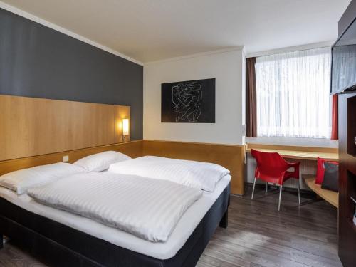 a bedroom with a bed and a desk and a red chair at ibis Kassel Melsungen in Melsungen
