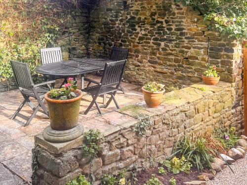 a table with two chairs and two potted plants on a stone wall at Causeway Cottage in Wolsingham