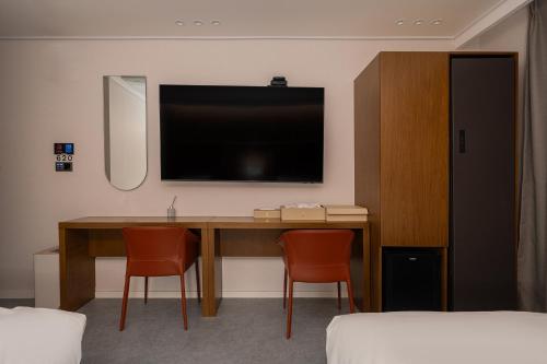 a room with a desk with two chairs and a television at Browndot Incheon Airport New City in Incheon