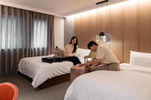 a man and woman sitting on beds in a hotel room at Browndot Incheon Airport New City in Incheon