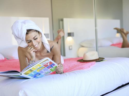 a woman laying on a bed reading a book at Ibis Styles Menton Centre in Menton