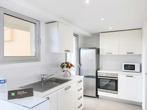 a white kitchen with a sink and a refrigerator at Ibis Styles Menton Centre in Menton