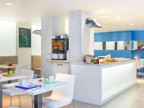 a kitchen with white counters and white tables and chairs at Ibis Styles Menton Centre in Menton