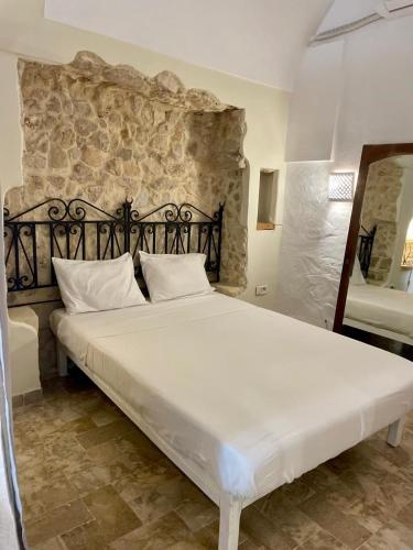 Una gran cama blanca en una habitación con una pared de piedra. en Casa Dea - Bungalow Apollon, en Hammamet Sud