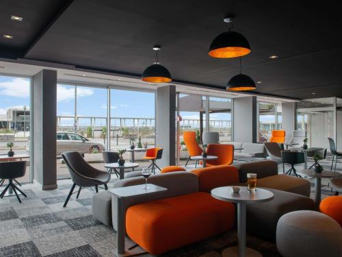 a waiting room with orange chairs and tables and windows at Mercure Dieppe La Présidence in Dieppe
