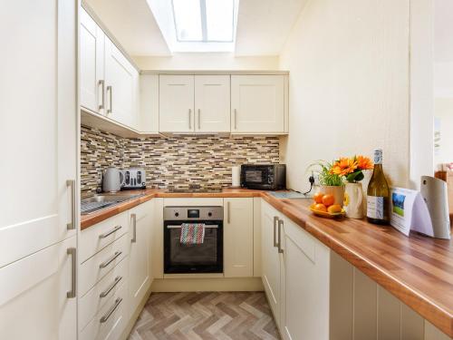 eine Küche mit weißen Schränken und einer Holzarbeitsplatte in der Unterkunft Carraig Dhubh Cottage - Uk47123 in Whiting Bay