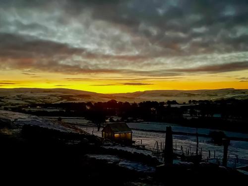 a sunset over a field with a barn in the foreground at Kinder in Mellor