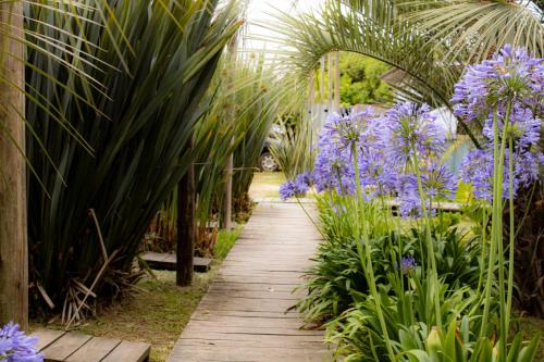 a wooden pathway through a garden with purple flowers at Las Luciernagas Posada de Mar in La Pedrera