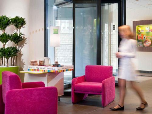 a woman walking through a room with pink chairs at ibis Styles Saint Dizier in Saint-Dizier