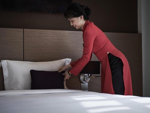 a woman is standing next to a bed at Mercure Hanoi La Gare Hotel in Hanoi