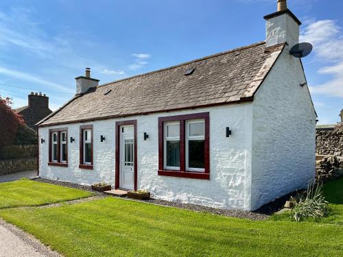Una cabaña blanca con ventanas rojas y un patio de césped. en Kilquhanity Cottage, en Castle Douglas