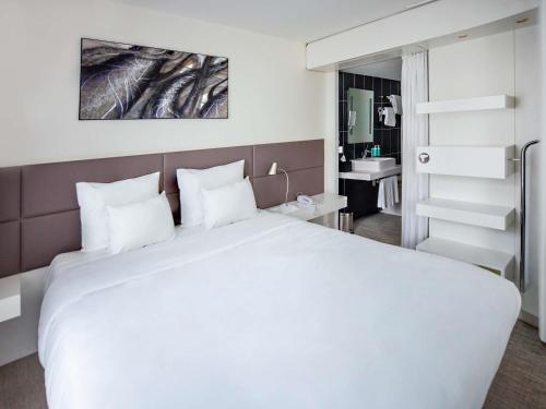 a bedroom with a large white bed and a bathroom at Novotel Suites Paris Issy Les Moulineaux in Issy-les-Moulineaux