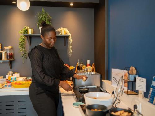 a woman standing in a kitchen preparing food at Novotel Suites Paris Issy Les Moulineaux in Issy-les-Moulineaux