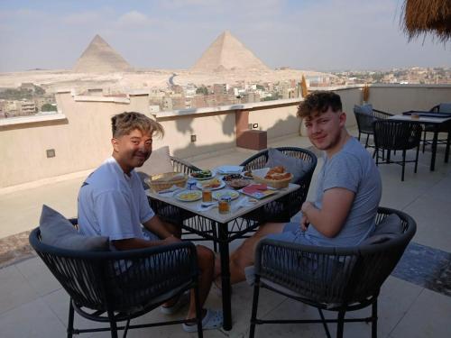 two men sitting at a table with food and the pyramids at Happy Day Pyramids View Hotel in Cairo