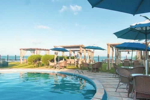 a swimming pool with chairs and umbrellas and a table and chairs at Pousada Praia das Tartarugas in Barra de Tabatinga
