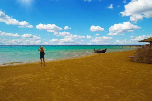 a woman standing on a beach with a boat in the water at Casa Mare Resort - ex, Royal Tulip Beach Resort in Port Ghalib