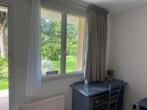 a room with two windows and a desk with a bottle of water at Logis Hôtel La Demeure du Perron in Quettehou