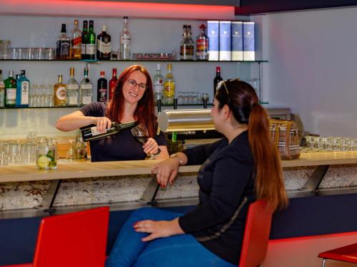 two women sitting at a bar with a bartender at ibis Stuttgart Airport Messe in Leinfelden-Echterdingen