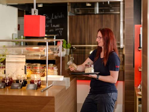 a woman standing in a kitchen holding a tray of food at ibis Stuttgart Airport Messe in Leinfelden-Echterdingen