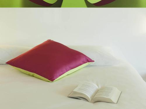 a red pillow and an open book on a bed at ibis Styles Bordeaux Saint Médard in Saint-Médard-en-Jalles