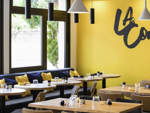 a restaurant with tables and chairs and a yellow wall at ibis Lille Lomme Centre in Lomme