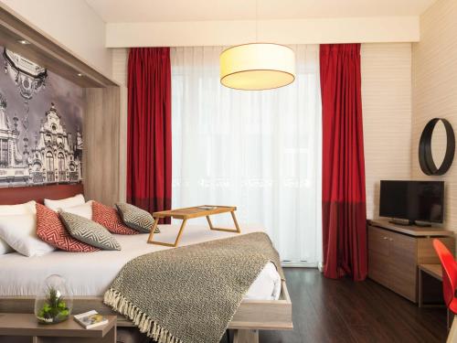 a bedroom with a bed with red curtains and a television at Aparthotel Adagio Brussels Grand Place in Brussels