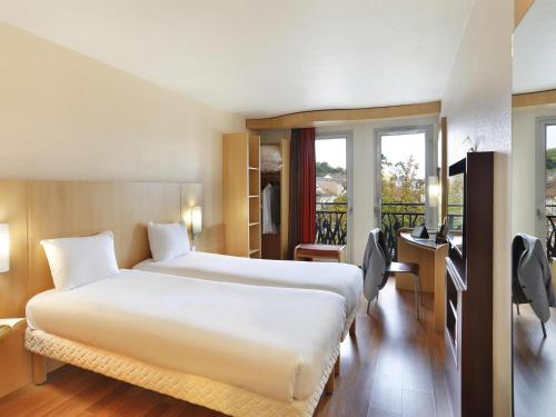 a hotel room with a bed and a desk and windows at ibis Etampes in Étampes