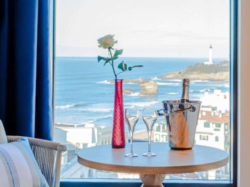 a table with two glasses and a bottle and a flower at Mercure Président Biarritz Plage in Biarritz