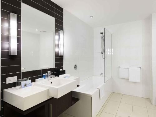 une salle de bain blanche avec un lavabo et une douche dans l'établissement Novotel Brisbane Airport, à Brisbane