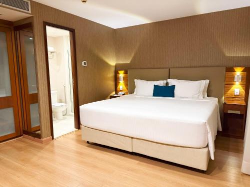 a bedroom with a large white bed and a bathroom at Wyndham Sao Paulo Ibirapuera Convention Plaza in Sao Paulo