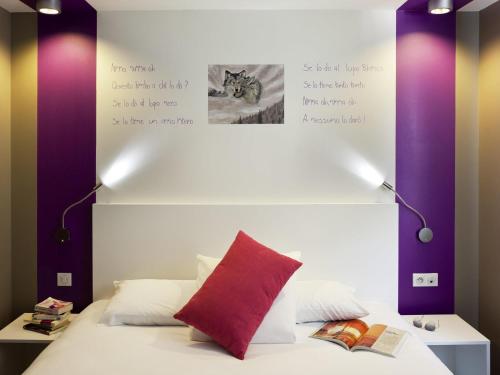 a bed with a red pillow and two lights at ibis Styles Rennes St. Gregoire in Saint-Grégoire