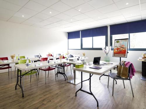 a room with white tables and chairs and windows at ibis Styles Rennes St. Gregoire in Saint-Grégoire