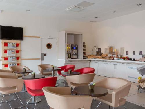 a restaurant with tables and chairs and a kitchen at Hôtel ibis Guingamp Cœur de Bretagne in Ploumagoar