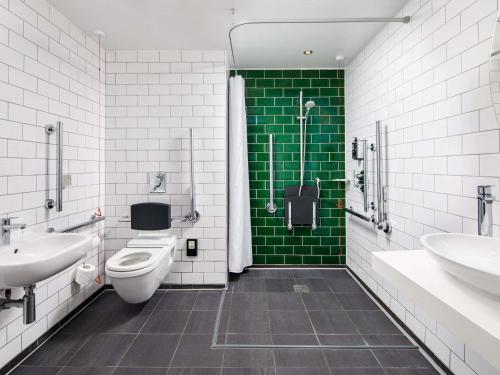 a bathroom with two sinks and a toilet and green tiles at ibis Styles London Southwark - near Borough Market in London